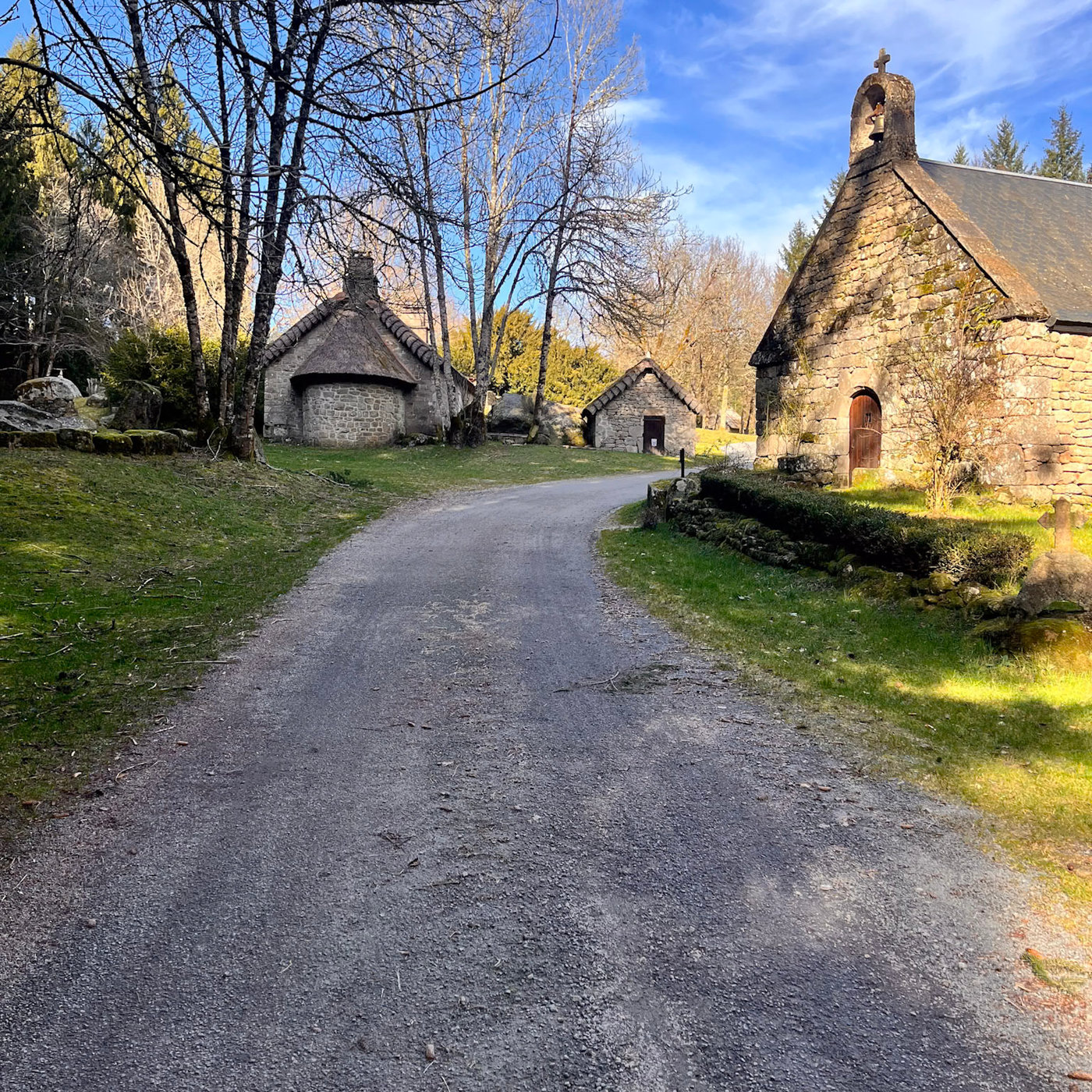 Maisons de pierre et petite chapelle du hameau abandonné de Clédat en Corrèze, entourées d'arbres et de prairies sous un ciel bleu.