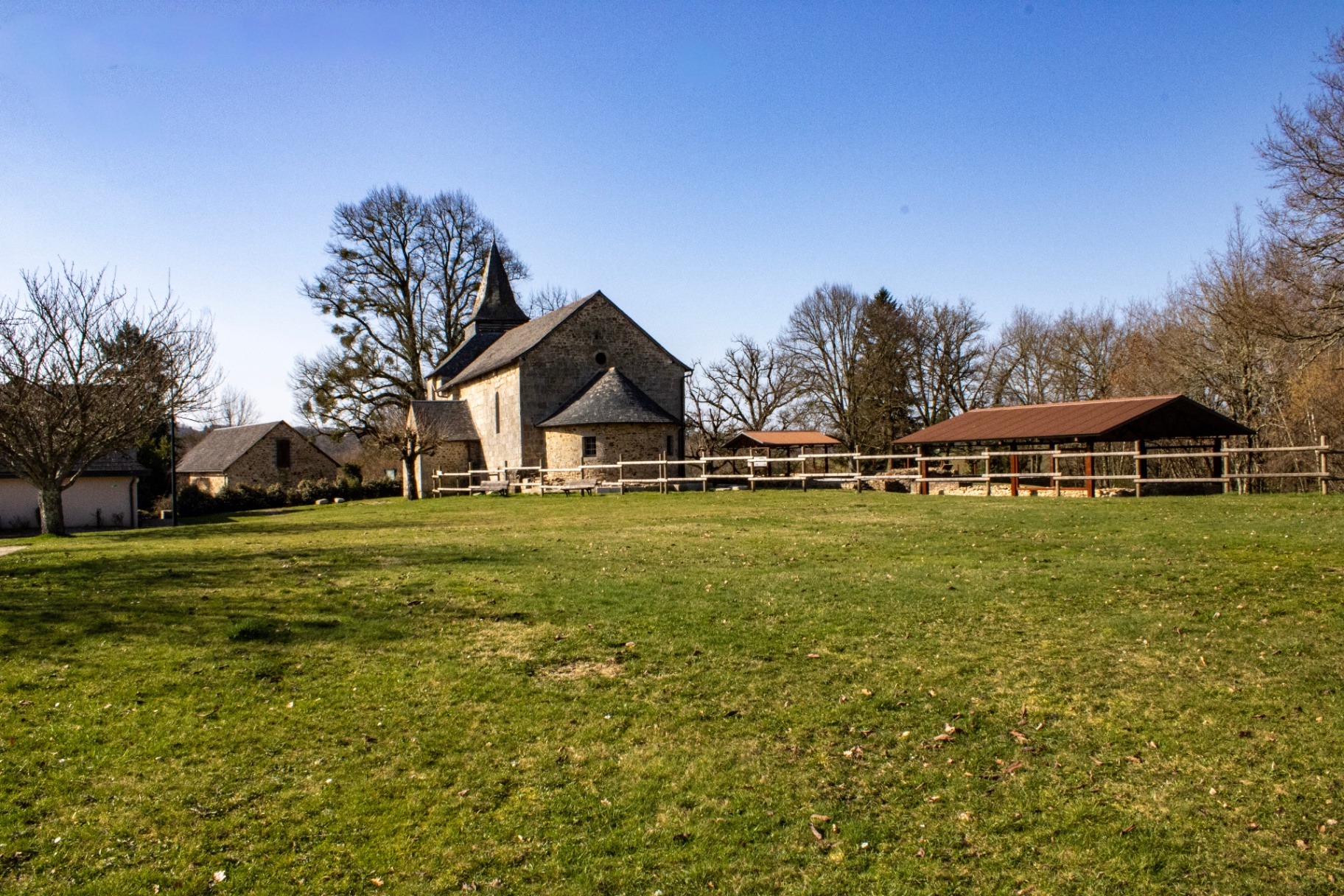 Église templière romane en pierre de Soudaines-Lavinadière en Corrèze, avec clocher à flèche, au milieu d'un pré verdoyant sous un ciel bleu.