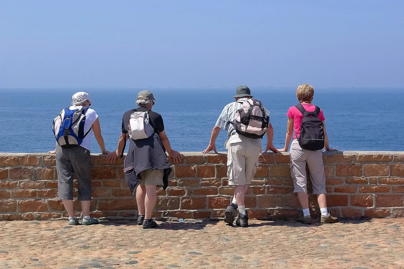 Groupe de marcheurs avec sacs à dos accoudés à un muret de pierre face à la mer, sur l'île de Bréhat en Bretagne — balade lente et accessible en famille.