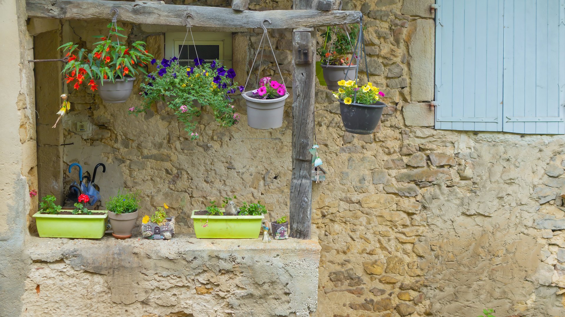 Maison de pierre traditionnelle française aux volets bleus, entourée de fleurs, dans un village de campagne — hébergement écoresponsable en France.