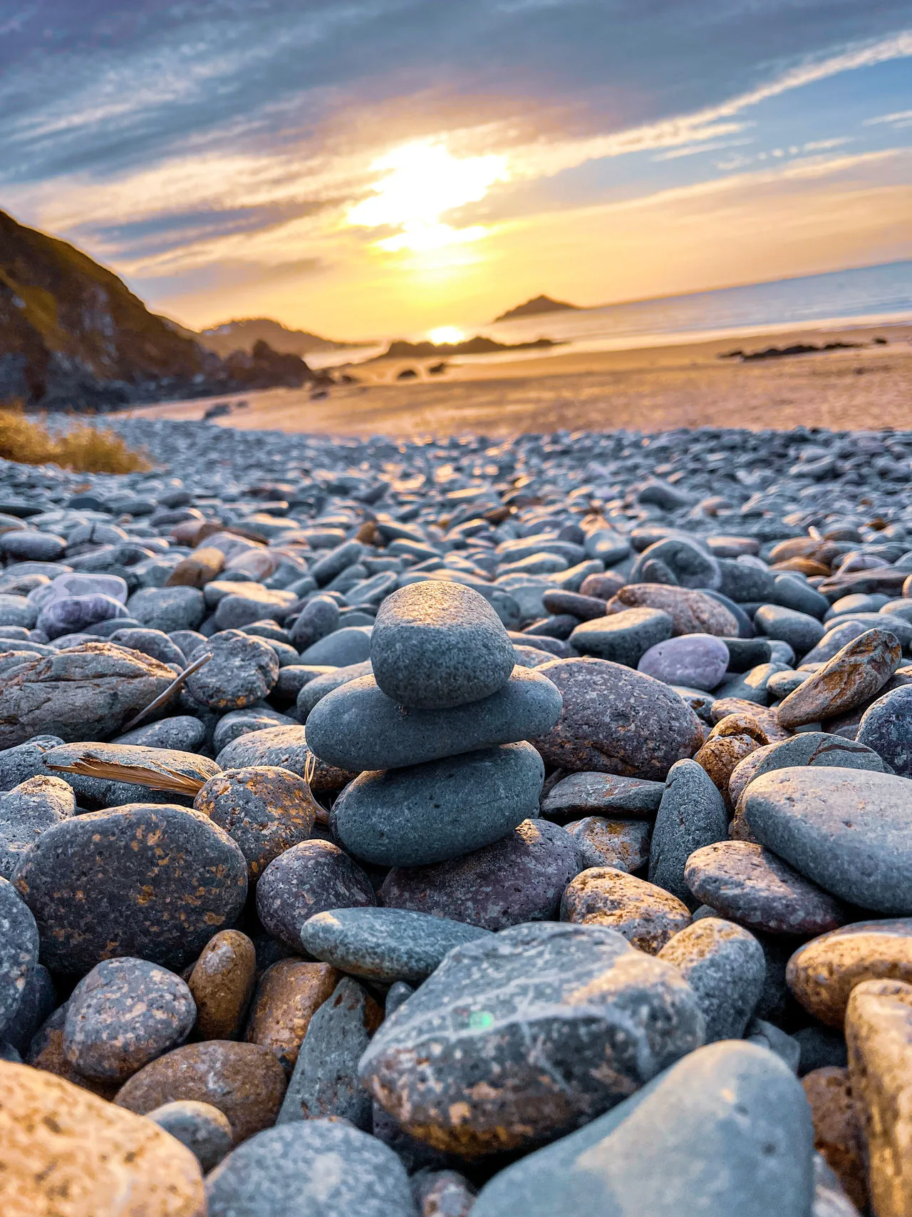 Galets empilés sur une plage au coucher du soleil, illustrant un séjour court plus apaisé, équilibré et ressourçant.