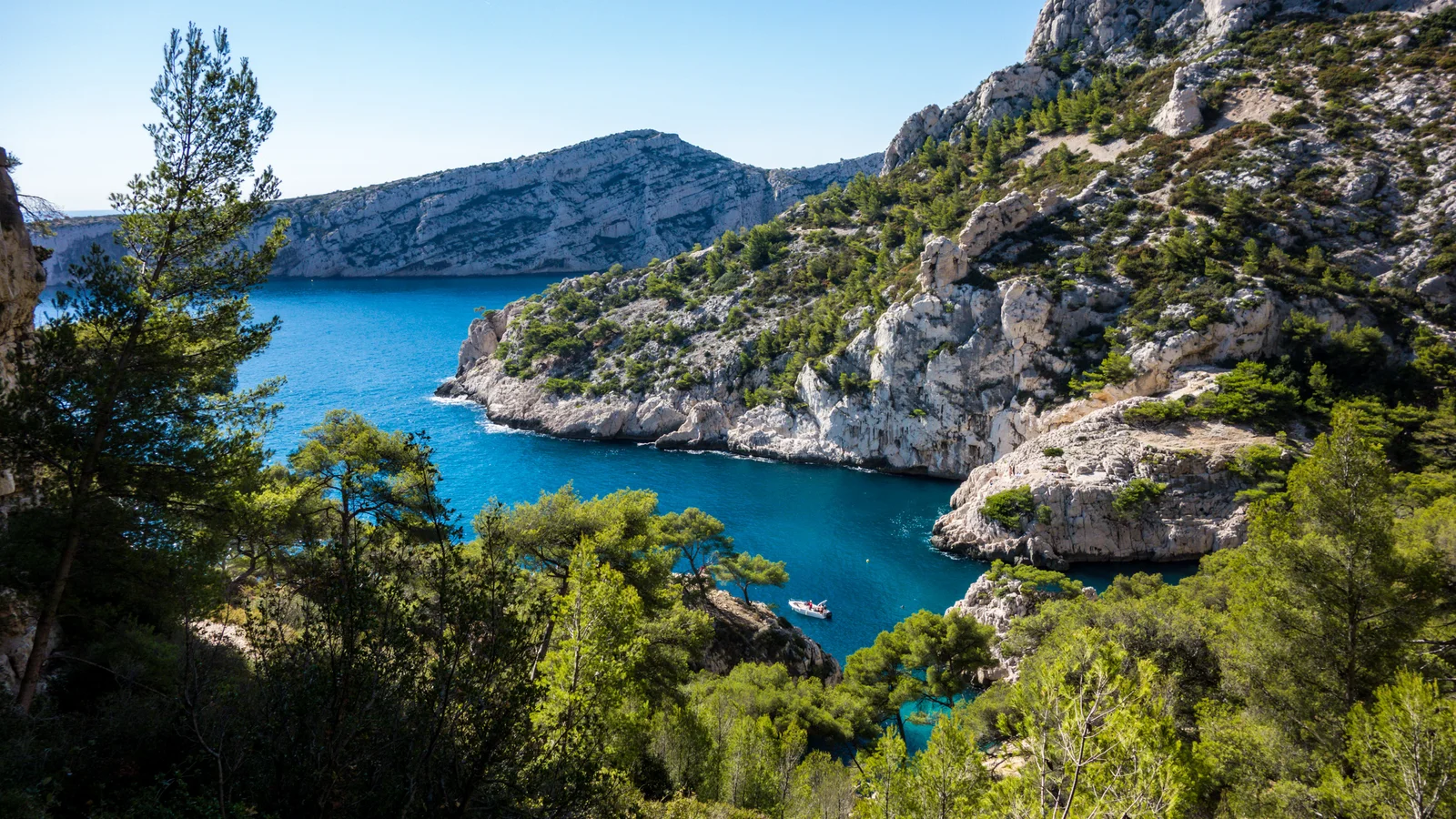 Vue plongeante sur la Calanque de Sugiton et son rocher du Torpilleur (Pierres-Tombées), falaises calcaires blanches, mer turquoise et pins d'Alep — Parc national des Calanques, Marseille.