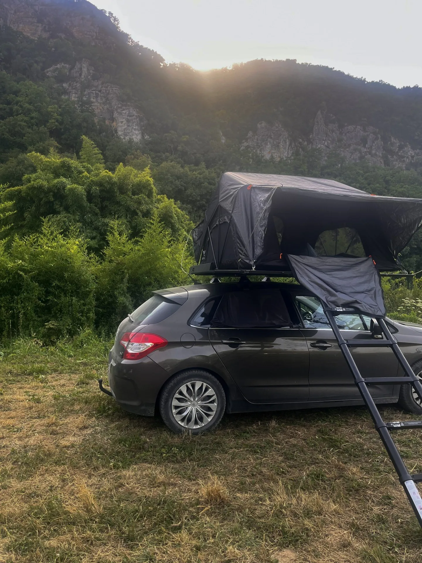 Voiture équipée d'une tente de toit installée au coucher du soleil face à un cirque rocheux en France — road trip nature et bivouac responsable au féminin.